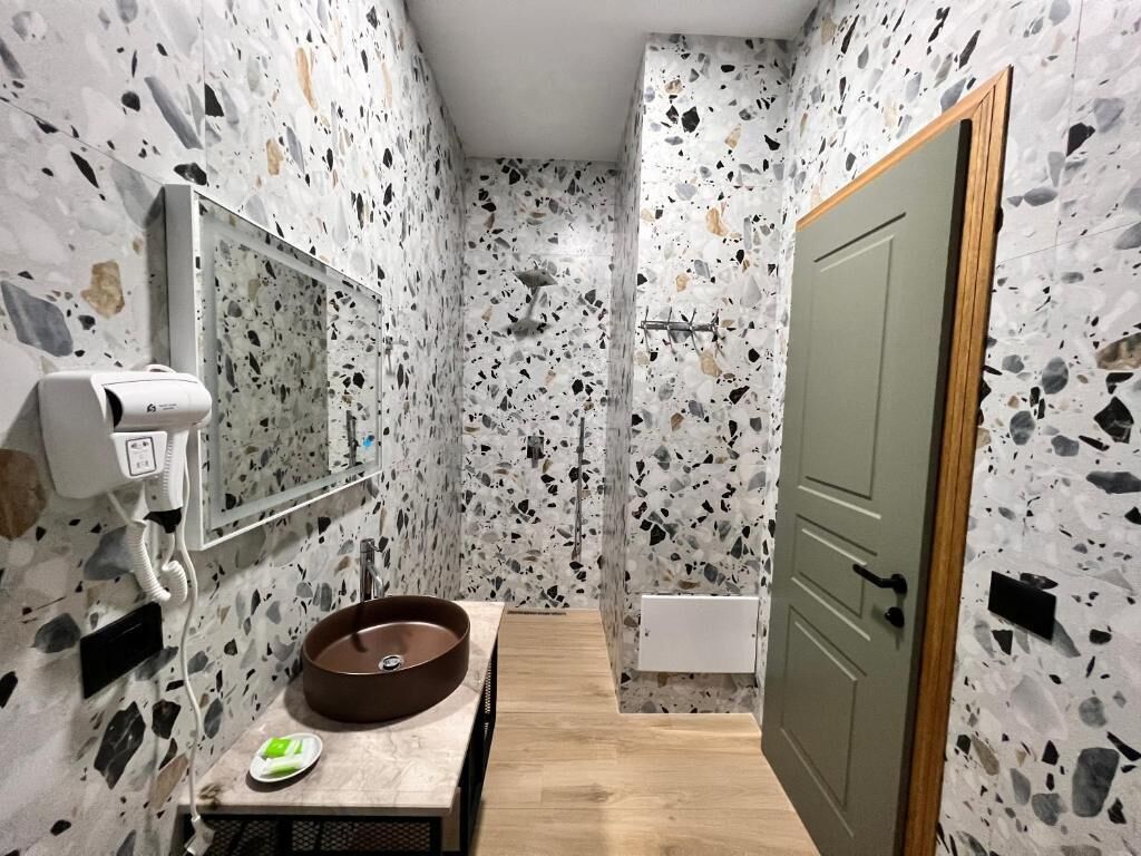 Un baño con suelo de terrazzo, un lavamanos redondo, un espejo y un perchero para toallas.