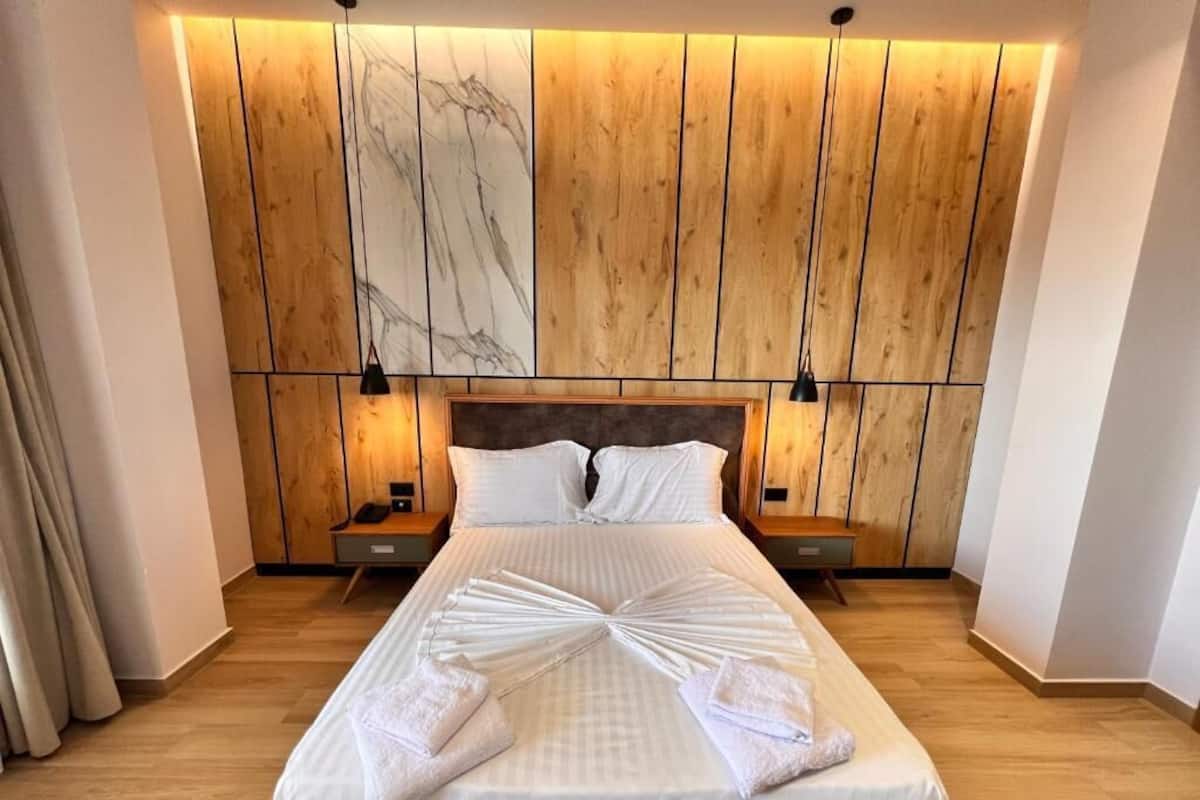 Un lit bien fait, avec des serviettes, une tête de lit en bois et deux tables de chevet avec des lampes.