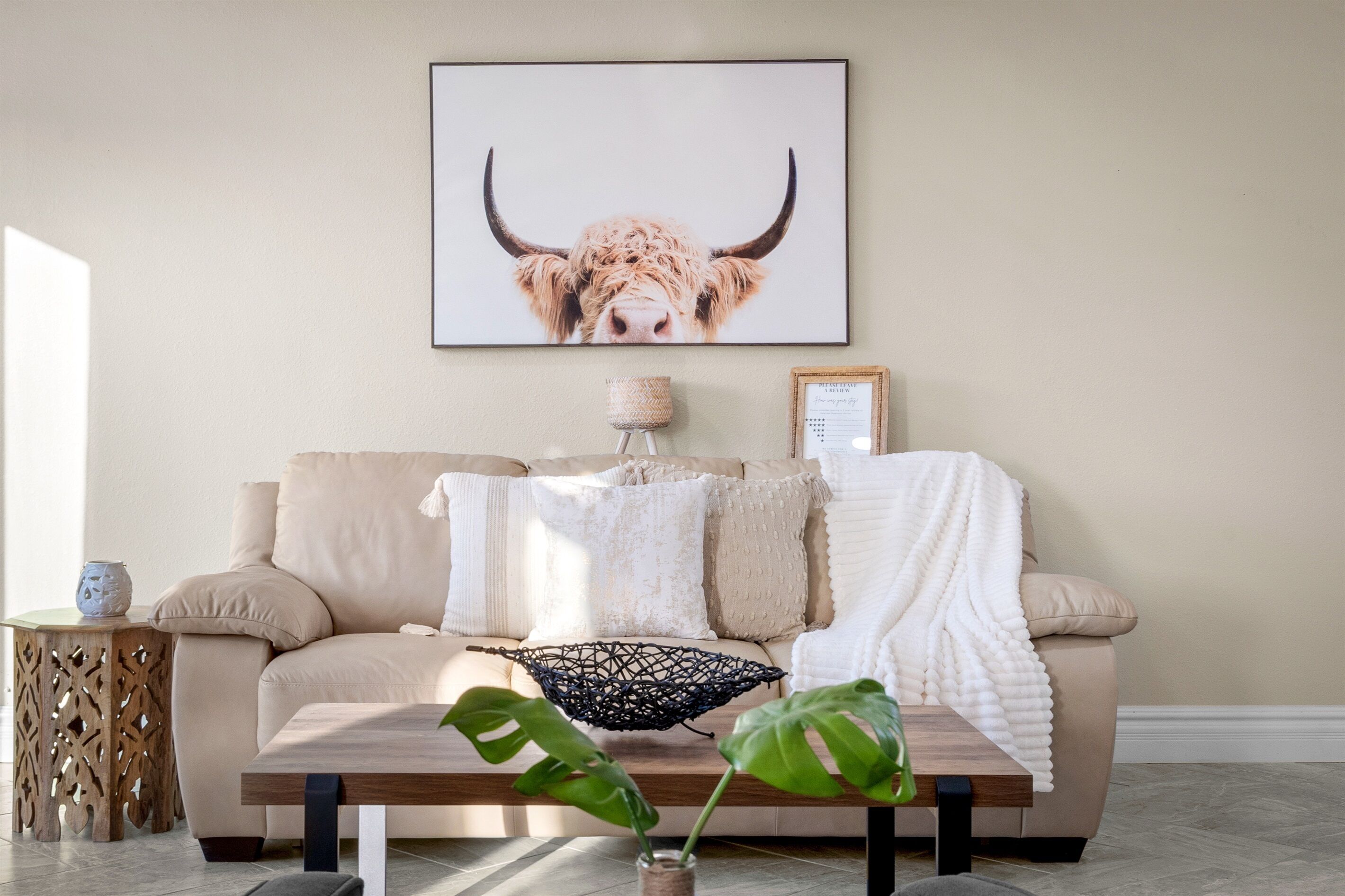 A living room with a beige sofa, a coffee table, and a framed artwork of a bull's head on the wall.