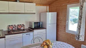 A compact kitchen with a microwave, refrigerator, sink, and a table with fruit.