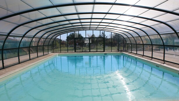 A covered swimming pool with a curved roof and clear glass panels.