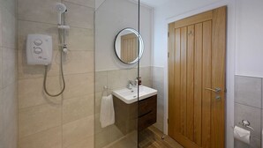 A modern bathroom with a glass-enclosed shower, a wooden door, a white sink, and a mirror. - Mrs Watermelon Apartment (Fort William)