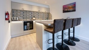 A modern kitchen with a central island, bar stools, and a decorative backsplash. - Mrs Watermelon Apartment (Fort William)