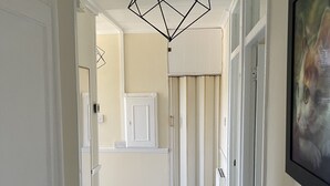 Un pasillo con una lámpara colgante de diseño geométrico, puertas blancas y un cuadro en la pared.