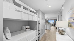 Een moderne hotelkamer met een stapelbed, een bureau met lamp, uitzicht op zee en een kitchenette.