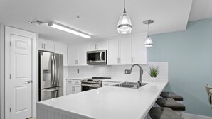 Een moderne keuken met witte kasten, roestvrijstalen apparatuur, een centraal kookeiland met barstoelen en hanglampen.