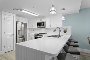 A modern kitchen with white cabinetry, stainless steel appliances, a central island with bar stools, and pendant lighting.