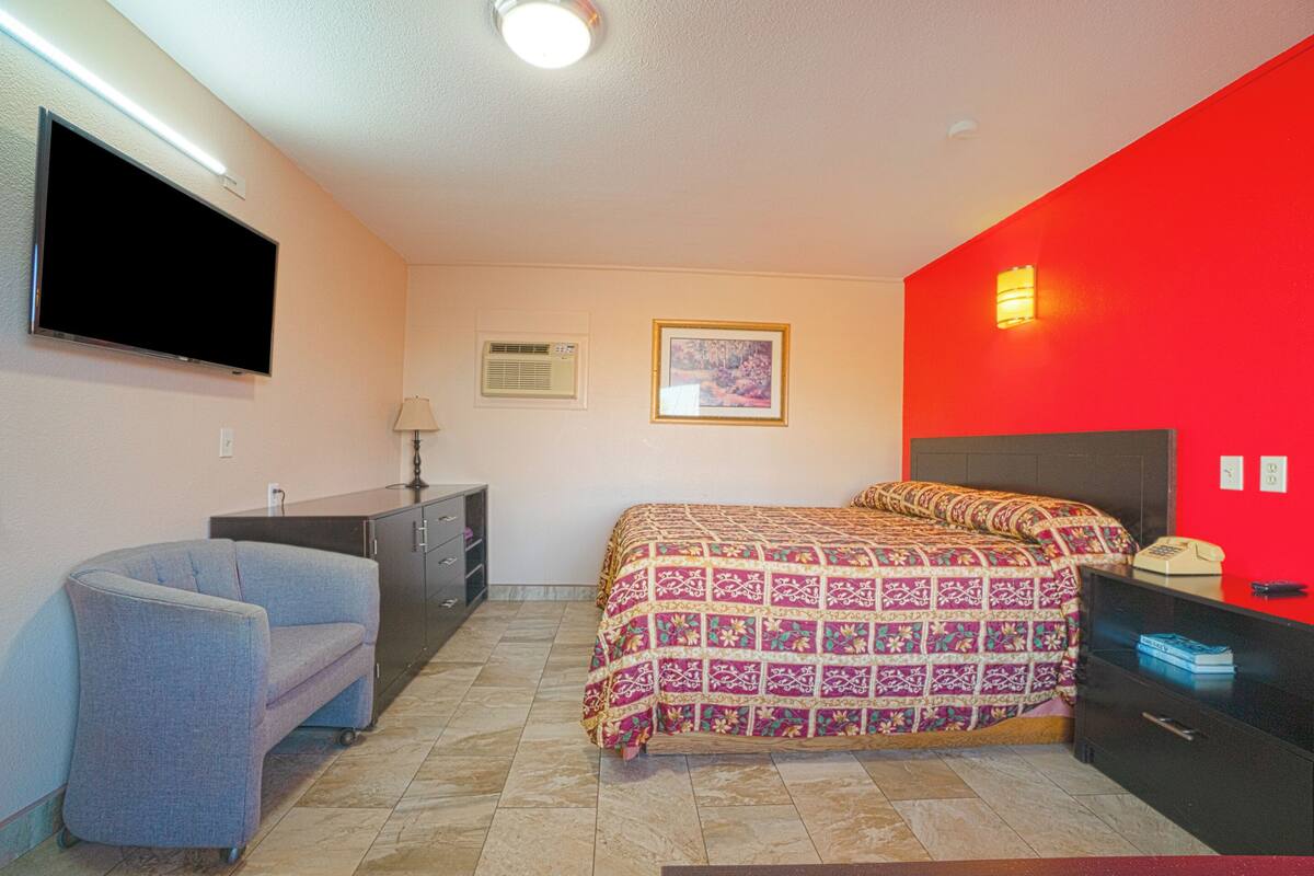 Un dormitorio con cama, una silla, un escritorio, un televisor y una pared de acento roja.
