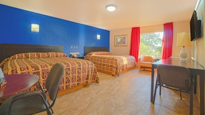 A hotel room with two beds, a desk, a chair, and a TV.
