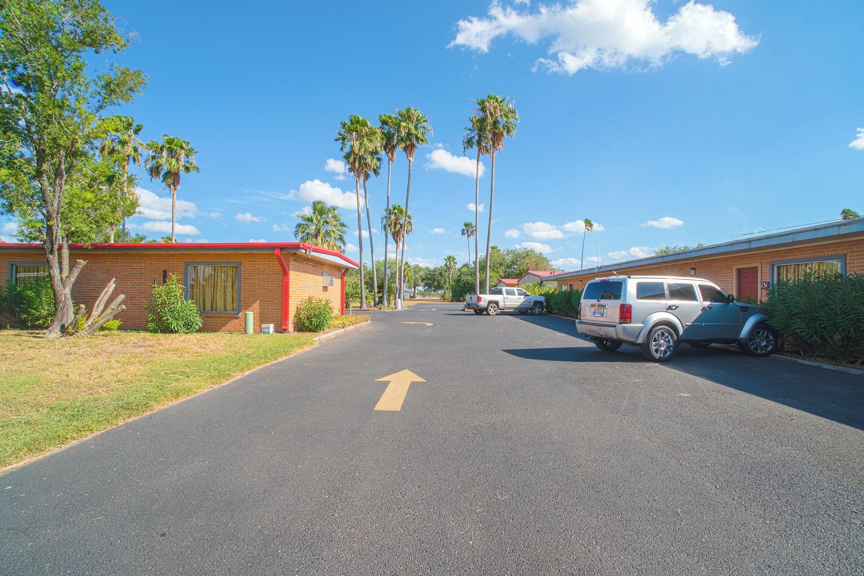 A street with a clear road marked with an arrow, surrounded by buildings and palm trees.