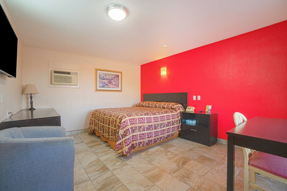 Una habitación con cama, escritorio, silla y una pared de acento roja.