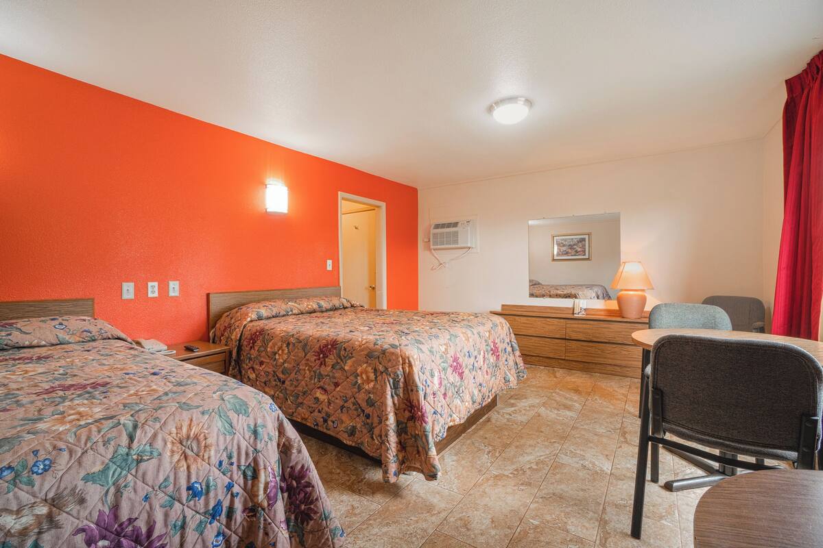 Habitación de hotel con dos camas, un escritorio, una silla, una lámpara y un aparador.