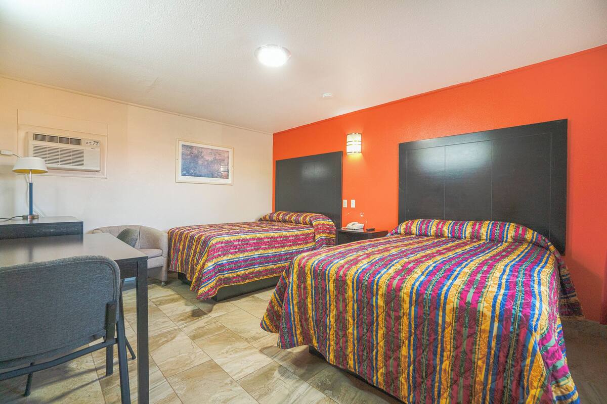 Una habitación de hotel con dos camas, un escritorio, una silla y una mesita de noche.