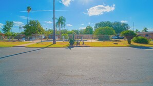 A parking lot with a clear sky, palm trees, and a building in the background.
