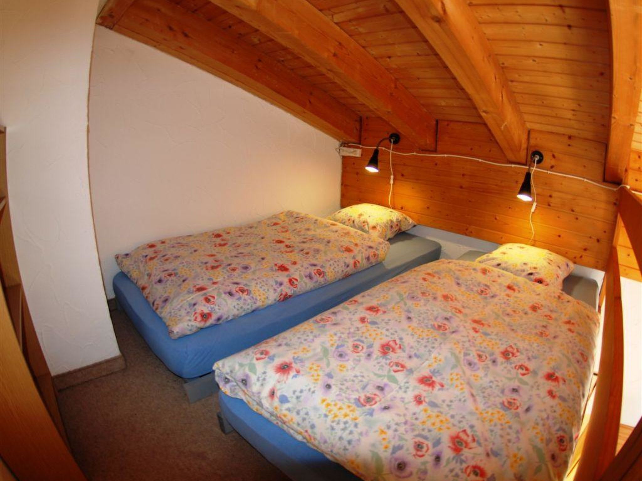 Ein kleiner, gemütlicher Raum mit zwei Einzelbetten, Holzbalkendecke und schlichtem, zweckmäßigem Design.