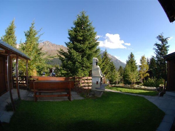 A well-maintained outdoor area with a wooden bench, a stone structure, and a mountain backdrop.