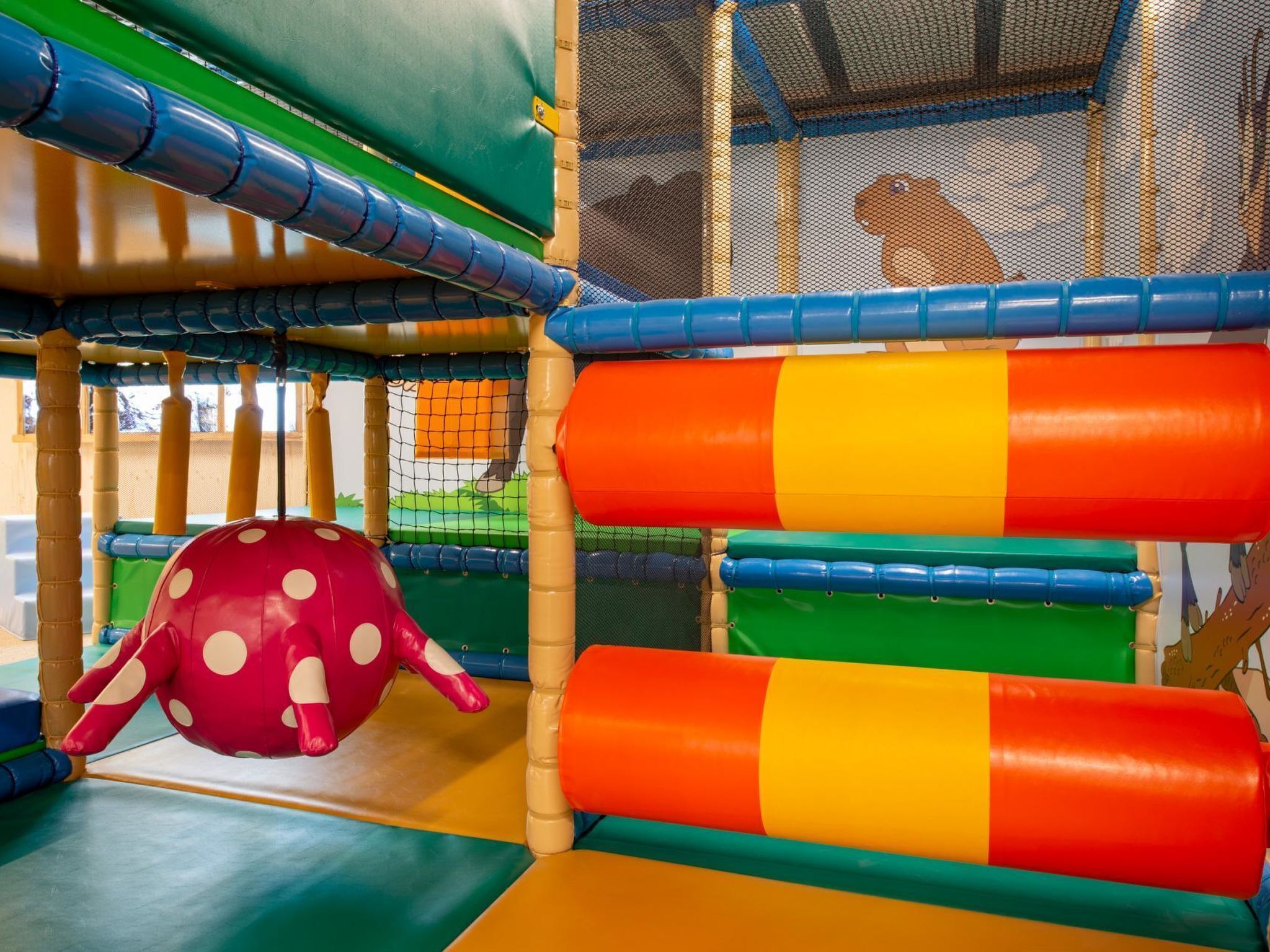 Een speelruimte met kleurrijke, gepolsterde constructies en een omheining van net.