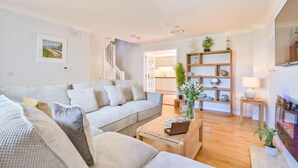Un salon avec un canapé, une table basse et un téléviseur. Un escalier mène à une autre pièce.