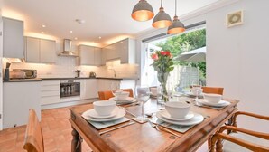 Une cuisine moderne avec des meubles blancs, une table à manger pour quatre personnes et des luminaires suspendus au-dessus.