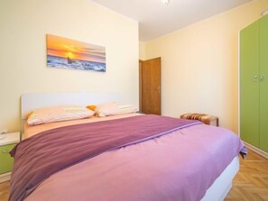 Une chambre à coucher avec un lit, une table de chevet, une armoire verte et un tableau représentant un coucher de soleil sur l’océan.