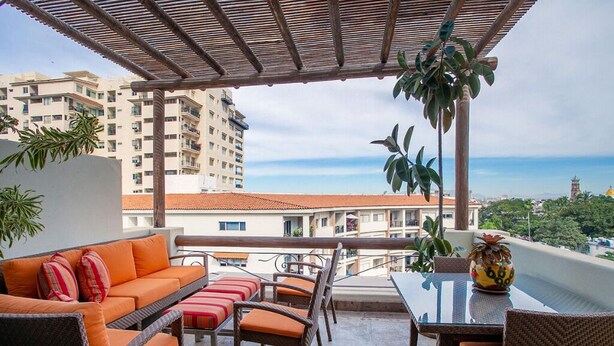 A balcony with wicker furniture, a glass table, and a potted plant.
