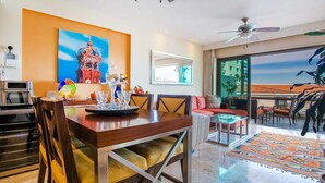 A modern living room with a dining area, large windows, and a view of the beach.