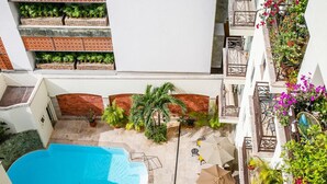 A rooftop pool area with a clear blue pool, surrounded by potted plants and outdoor furniture.