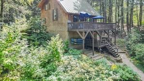 A cabin with a deck, surrounded by dense forest.