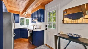 A modern kitchen with dark blue cabinets, a stainless steel refrigerator, and a wooden ceiling.