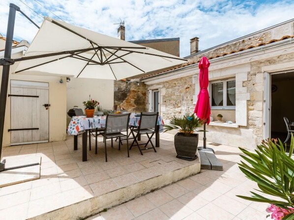 An outdoor patio with a table and chairs, a large umbrella, and a potted plant. - Les Rosiers by Interhome (Arvert)