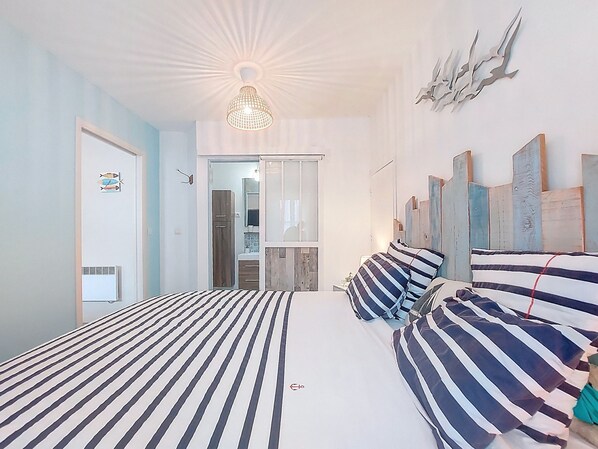 A bedroom with two beds, a ceiling light, a mirror, and a door.