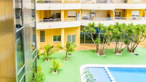 A multi-story hotel with a rooftop pool area, surrounded by greenery and palm trees.