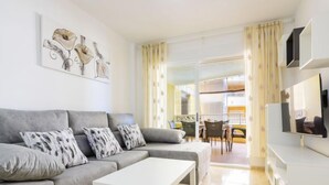 A modern living room with a grey sofa, white coffee table, and a dining area with a table and chairs.