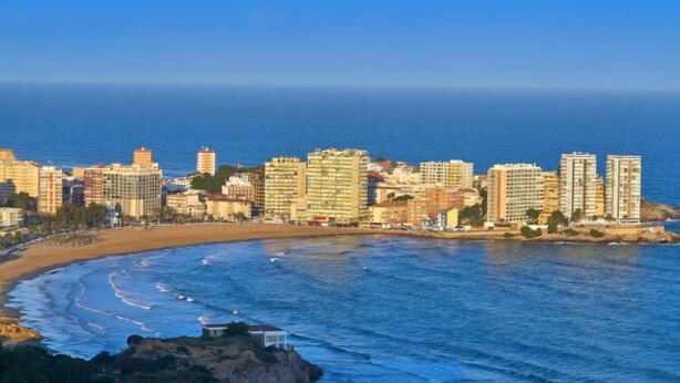 A coastal cityscape with high-rise buildings, a beach, and a rocky outcrop.