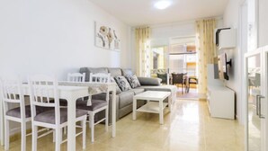A modern living room with a sofa, dining table, chairs, and a TV.