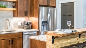 Eine moderne Küche mit Holzausbau, einem Edelstahlkühlschrank, einer Kaffeemaschine und einer Holzbank mit einer Zeitschrift.