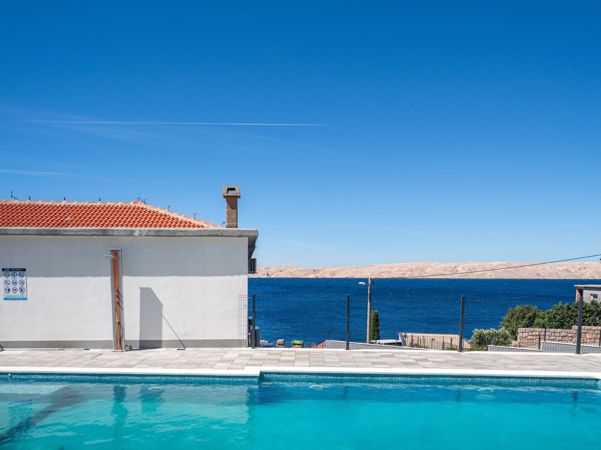 Una piscina con vista despejada al mar, un edificio con tejado de cerámica y un paisaje arenoso al fondo.
