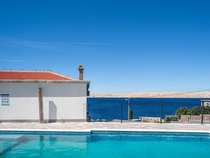 A swimming pool with a clear view of the sea, a building with a tiled roof, and a sandy landscape in the background. - Apartment Delfin by Interhome (Karlobag)