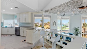 Una cocina moderna con armarios blancos, una isla central y vistas a palmeras afuera.