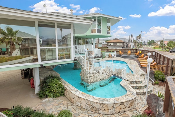 A modern house with a large glass window, a swimming pool, and a stone deck.