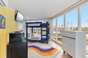 A room with a bunk bed, a desk, a dresser, and large windows offering a view of the neighborhood.