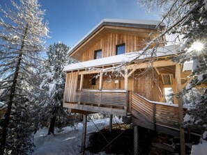A wooden cabin with a balcony, surrounded by snow-covered trees.