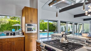 A modern kitchen with a built-in oven, a gas stove, and a large window overlooking a pool.