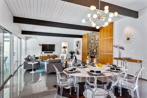 A modern living room with a dining area, a stone accent wall, and a large chandelier.