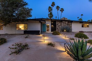 A modern house with a stone facade, large windows, and a well-lit entrance. - Aqua House - Luxury Midcentury Pool Retreat (Palm Springs)