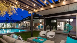 An outdoor patio with a pool, seating area, and a covered section with chairs and tables.