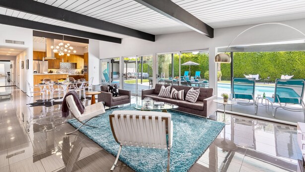 A modern living room with a glass coffee table, a sofa, and a chair. There is a view of a swimming pool outside.