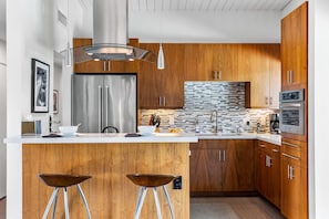 A modern kitchen with wooden cabinets, stainless steel appliances, and a central island with stools.