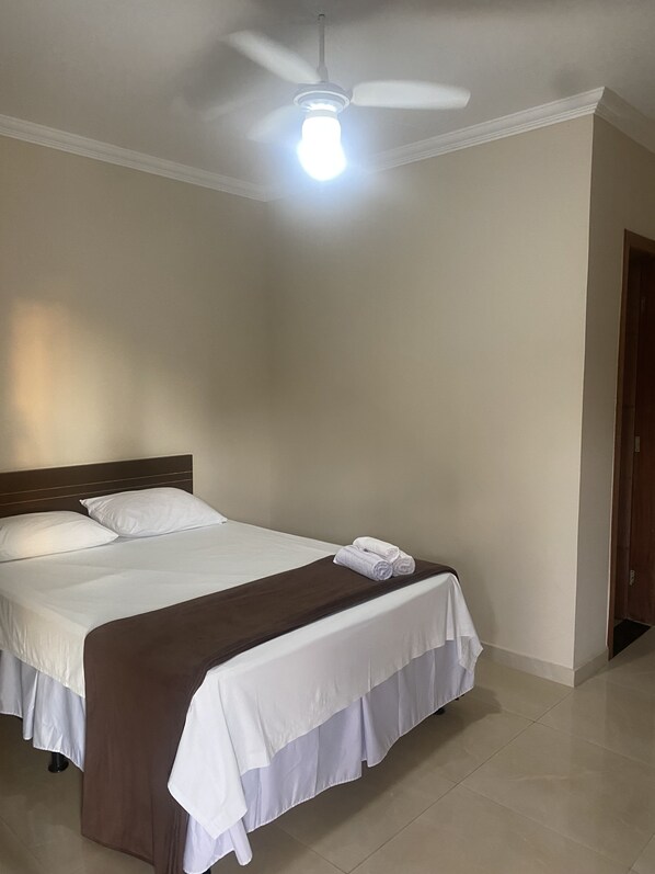 A hotel room with a bed, a ceiling fan, and a light fixture.
