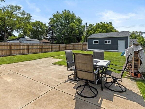 A backyard patio with a table and chairs, a covered grill, and a shed in the background. - Modern and Spacious Downtown House (Indianapolis)